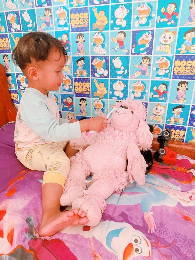 Toddler using a toothbrush to brush the teeth of a pink stuffed poodle toy.