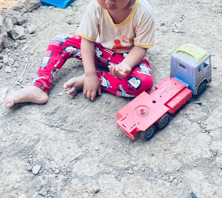 Close up of a toddler developing fine motor skills by examining small clumps of dirt in his hand.