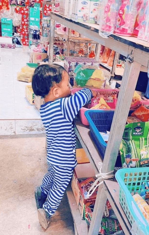 A toddler boy wearing blue and white striped pajamas exploring the bottom shelves of a grocery store aisle.