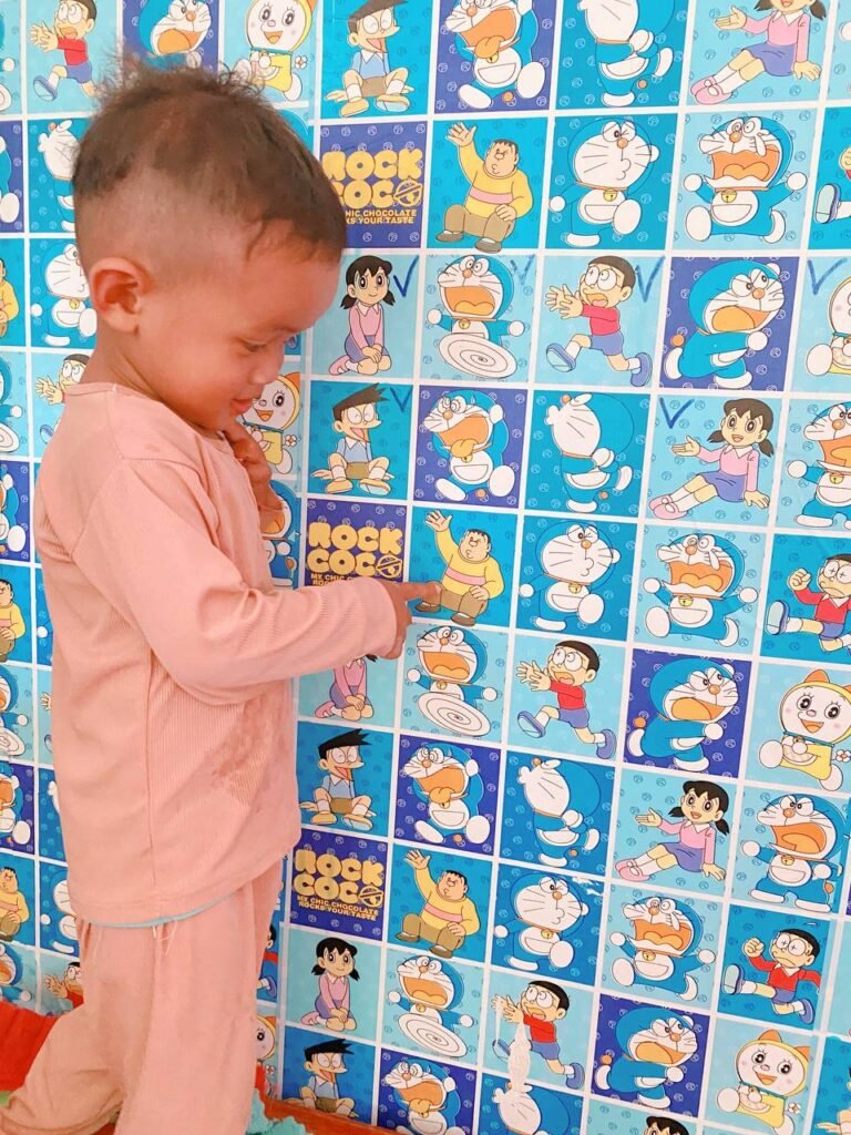A 2-year-old toddler pointing to colorful cartoon character decals on a playroom wall.