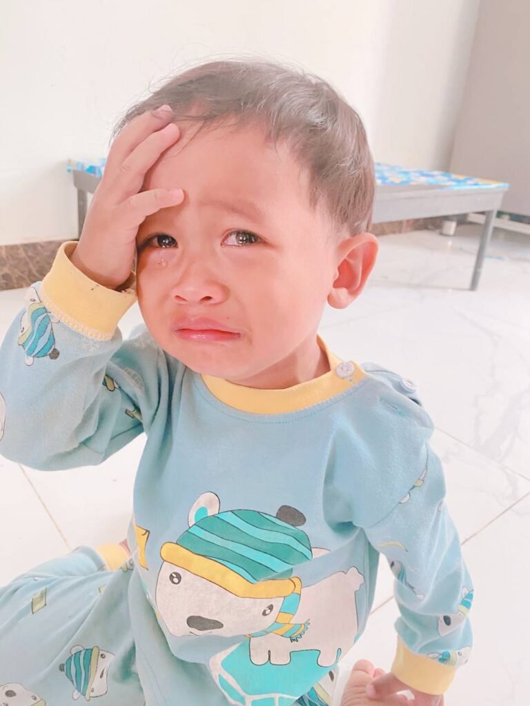 A stressed toddler boy holding his head in his hand during a meltdown over a missing toy.