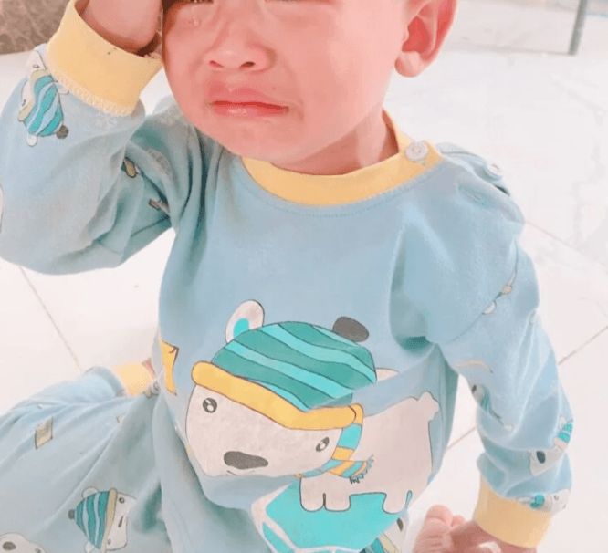 A stressed toddler boy holding his head in his hand during a meltdown over a missing toy.