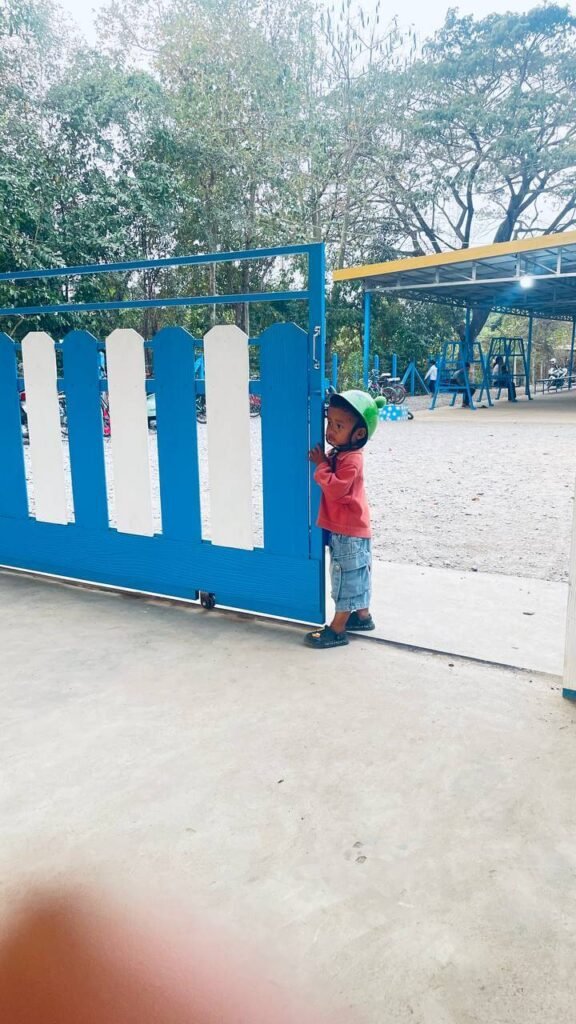 Toddler peeking through a blue metal gate at a park entrance.