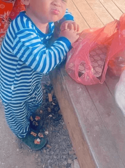 A toddler boy with squinted eyes and a scrunched nose making an angry protest face outside a store.