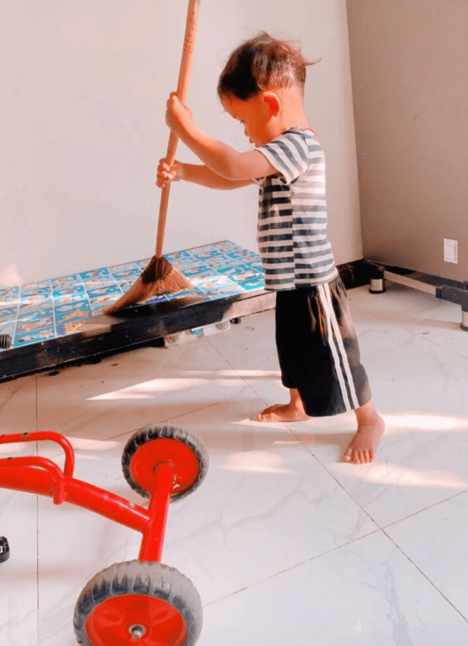 A 2-year-old boy sweeping the floor with a full-sized adult broom.