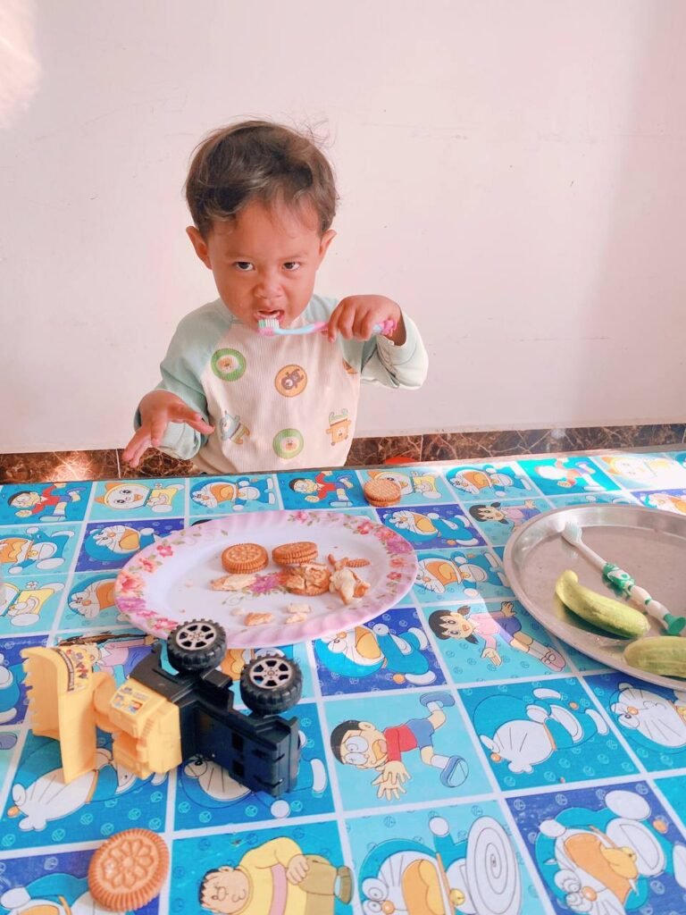 Toddler holding a soft toothbrush and eating cucumbers on a plate to relieve sore gums.
