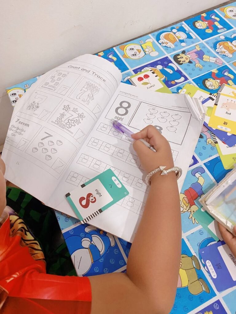 Close up of a child's hand using a purple pen to trace the word eight next to the number symbol in a workbook.