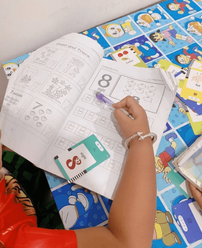 A bilingual flashcard showing a red snake shaped like the number 8 next to a workbook where a child is learning to read the word eight.