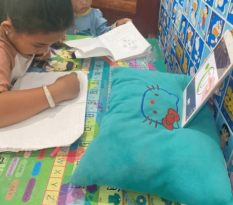 8-year-old girl focusing on homework at a small table while her toddler brother watches.