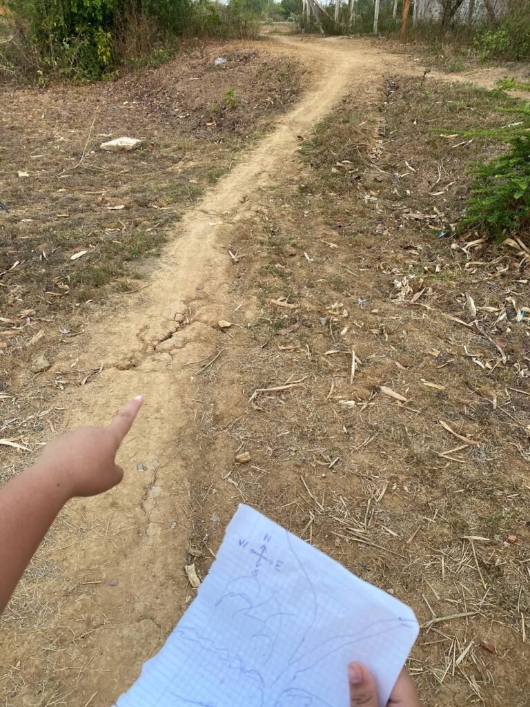 Child pointing down a clear dirt road while holding a hand-drawn map in her other hand.