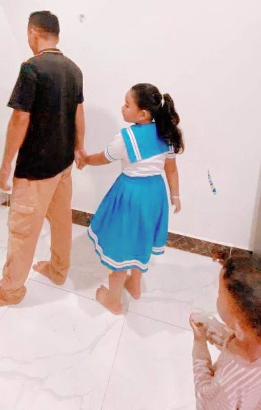 An older sister holding her father's hand to model safe behavior for her younger toddler brother.