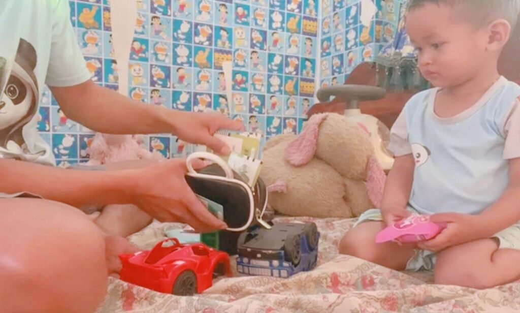 A parent sitting on the floor demonstrating how to pack flashcards into a black storage bag while their toddler watches.