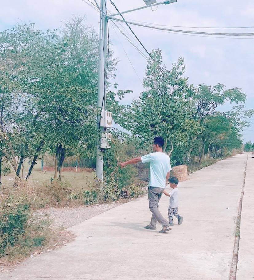 A father and toddler practicing holding hands while walking safely down a quiet, empty road.
