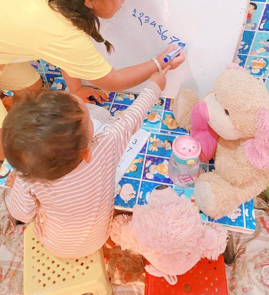 A young girl and her toddler brother pointing at numbers on a whiteboard together during a collaborative learning game.
