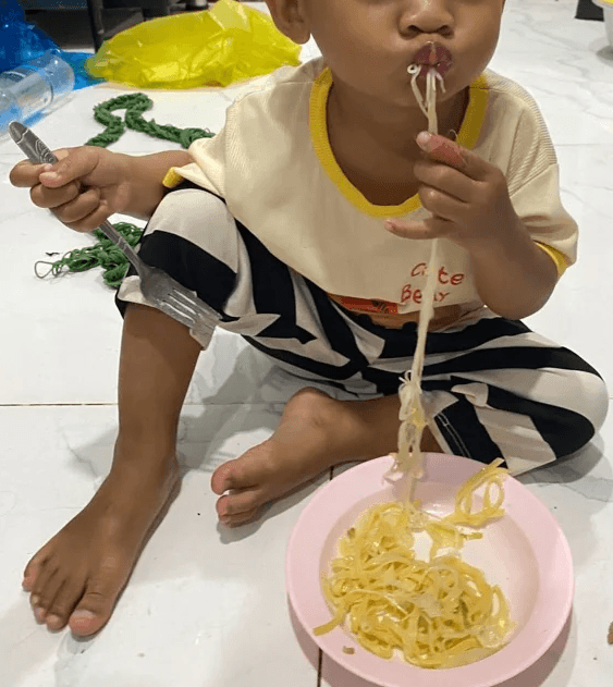 2-year-old boy eating noodles with a serious expression, refusing vegetables.