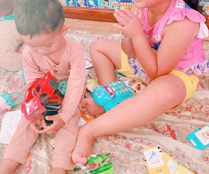 A young boy sitting calmly holding his red toy car after a sibling mediation, with his sister sitting peacefully beside him.