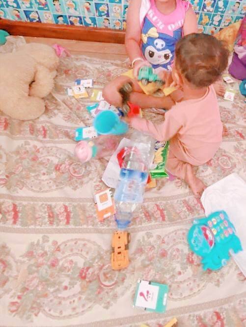 Toddler boy reaching for a green toy truck while his older sister plays with another toy next to a water bottle.