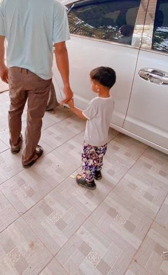 A father holding his two-year-old toddler's hand safely next to a parked car to practice parking lot rules.
