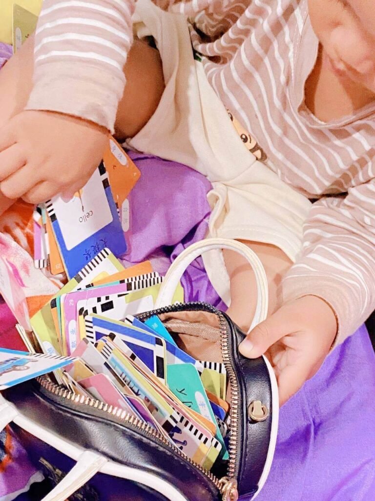 A toddler holding a black storage bag overflowing with vocabulary flashcards they tried to clean up.