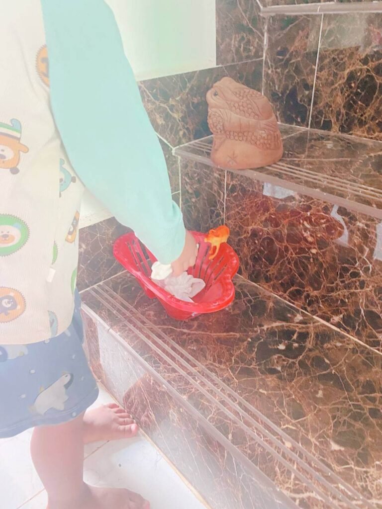 A toddler dropping a crumpled tissue into a small red basket strategically placed on a tiled staircase.