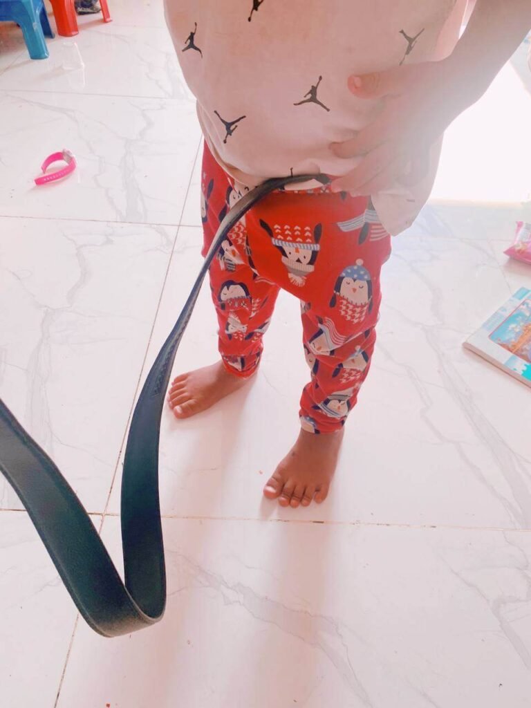A toddler's hands attempting to wrap a large black adult belt around their waist over their pajamas.