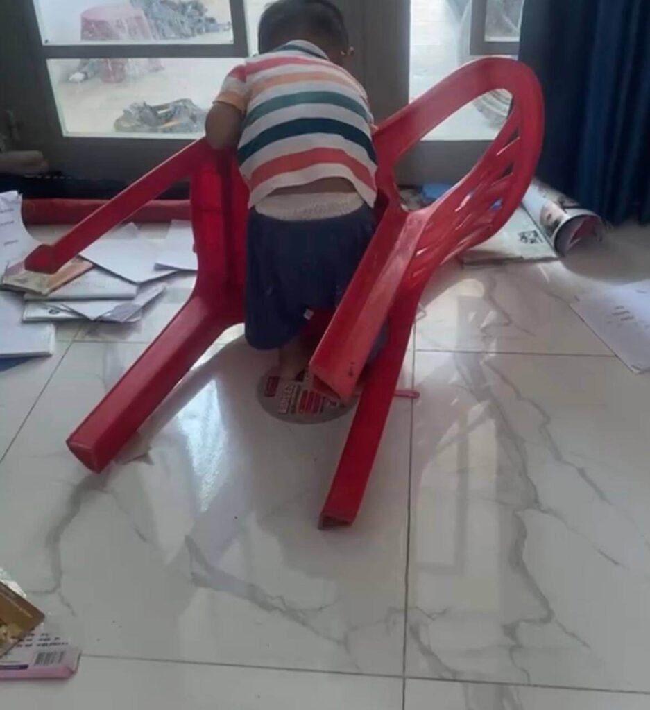 A toddler climbing inside the legs of an upside-down red plastic chair.