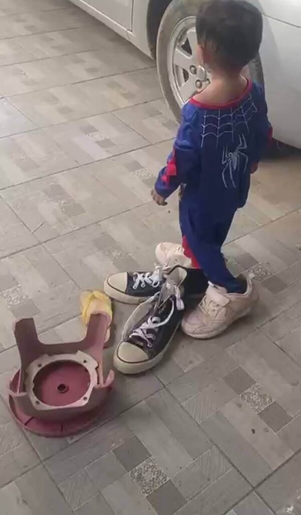 A toddler trying to walk outside while wearing oversized adult black sneakers over his own shoes.