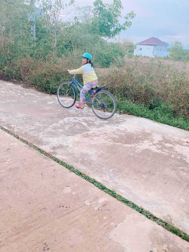 Young girl confidently riding an adult bike independently down a quiet, empty concrete path.