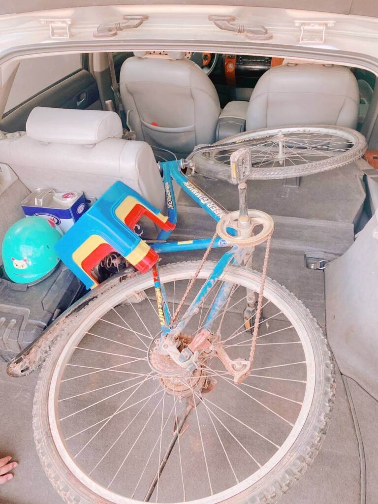 An adult bicycle, a green child's safety helmet, and a step stool packed into the trunk of a car for a safe riding lesson.