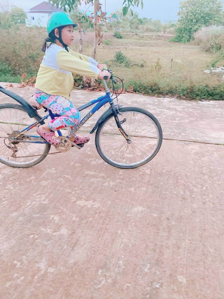 Determined young girl successfully pedaling an adult-sized blue bicycle after multiple failed attempts.