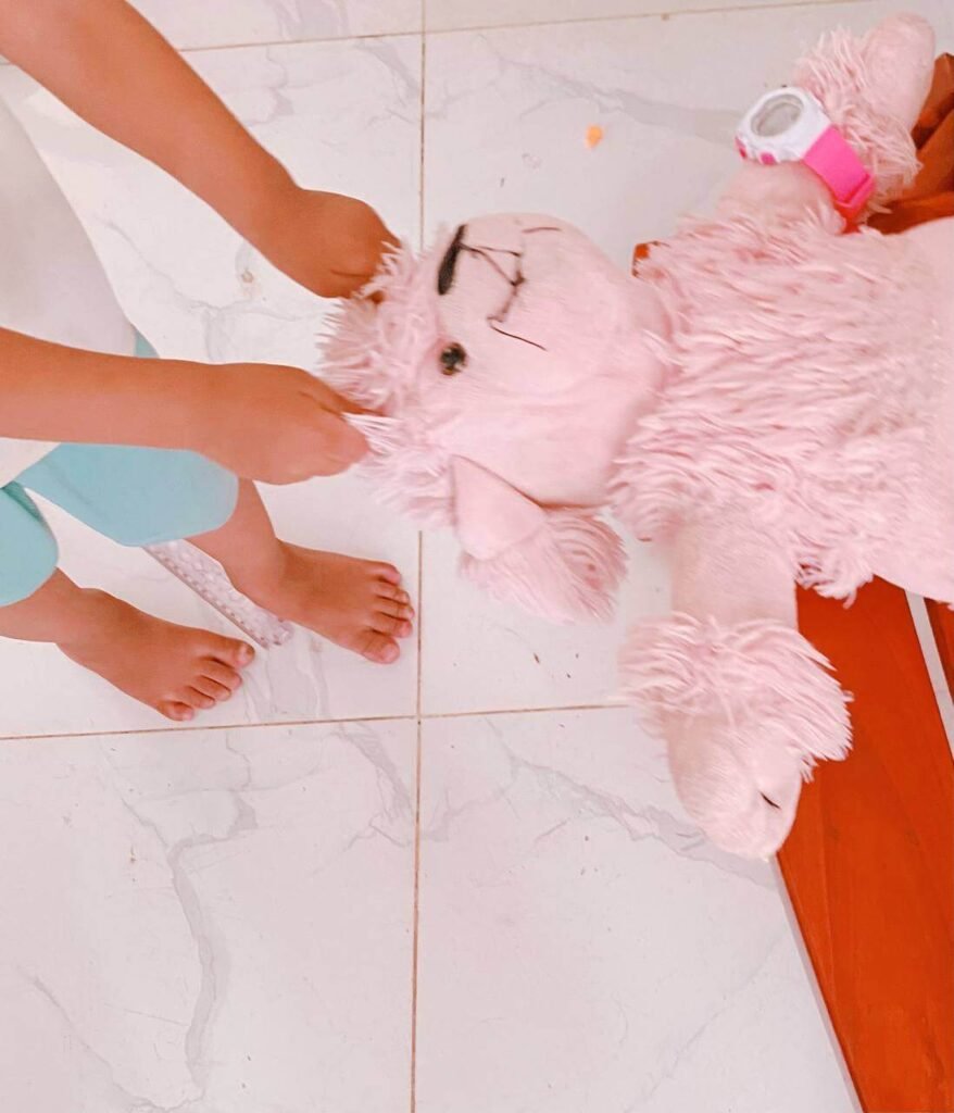 A toddler boy practicing his pretend hair washing skills on a fluffy pink poodle stuffed animal on a tiled floor.